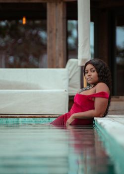 A stylish plus-size woman poses confidently by the poolside in a red dress.