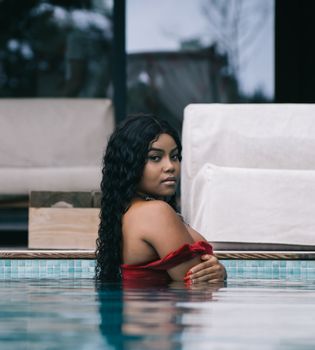 Sophisticated woman with long black hair posing gracefully in an outdoor pool setting, exuding elegance and confidence.