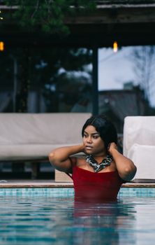 A woman with a necklace posing elegantly while relaxing in a swimming pool.