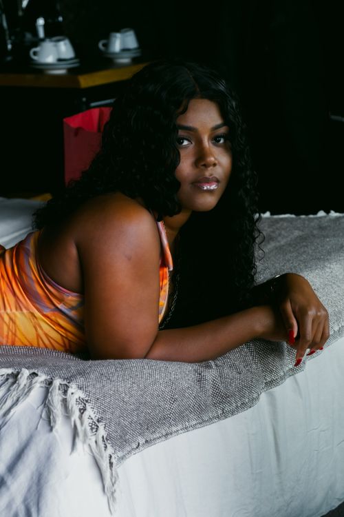 Free An African American woman with curly hair lying comfortably on a bed indoors. Stock Photo