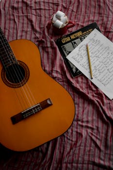 A warm setup with an acoustic guitar, coffee, and music notes on a striped bedspread.