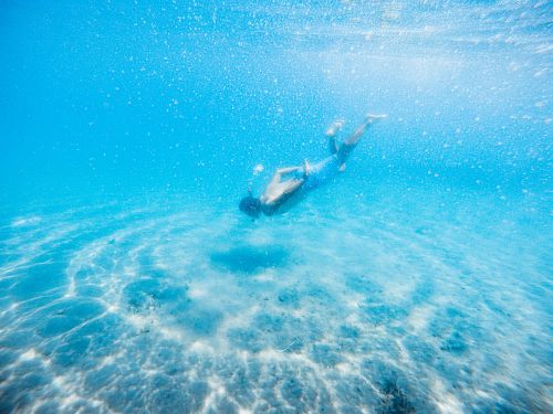 Free Side view of unrecognizable fit male traveler in oxygen mask and swimwear exploring colorful blue space under water in daylight Stock Photo