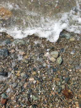 Close-up view of ocean waves crashing over a pebbled beach shore. Perfect for coastal themes.