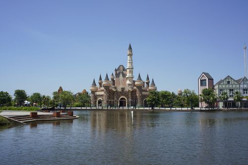 Free A picturesque view of a Disney-like castle reflecting on a serene pond under a clear blue sky. Stock Photo