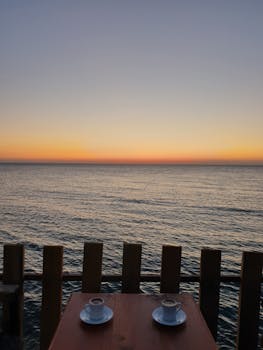 A tranquil scene of two coffee cups on a table overlooking the ocean at sunrise.