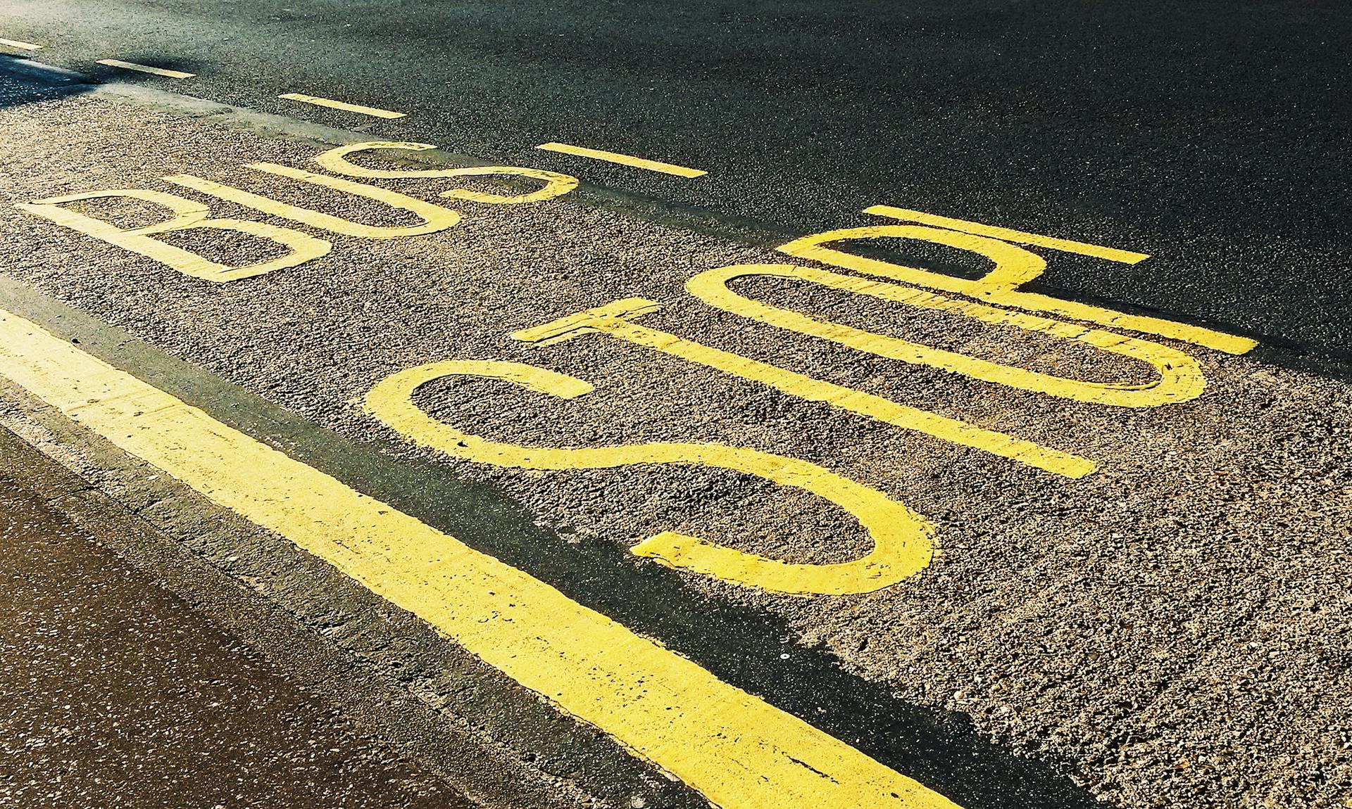 Close-up of a bus stop marking on an urban asphalt roadway with yellow lines.