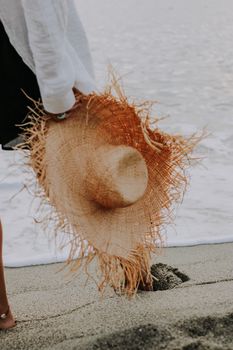 Close-up of a person holding a straw hat while walking along a sandy beach.