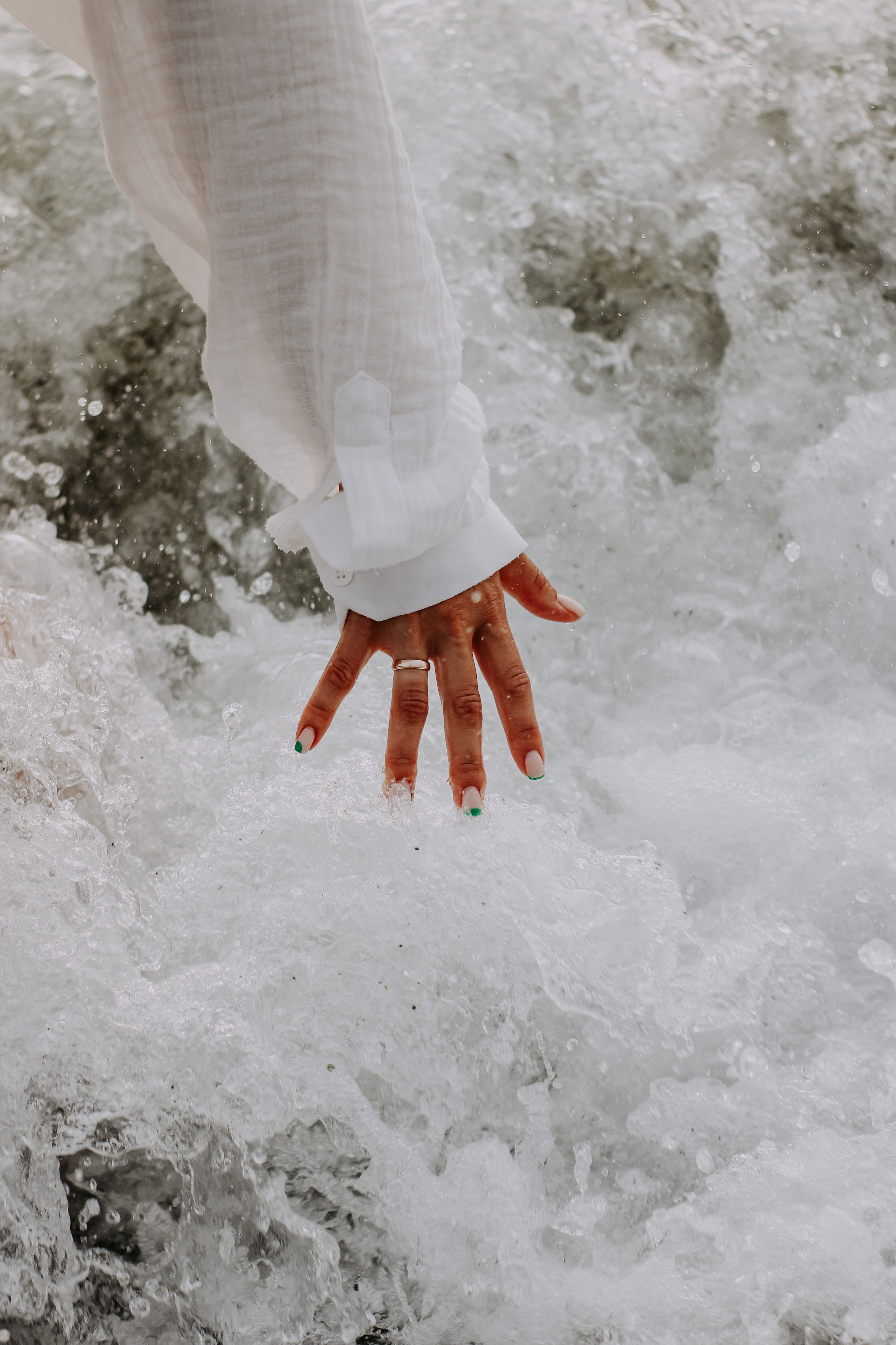 Close-up of a hand in a white sleeve touching ocean waves, creating a splash.