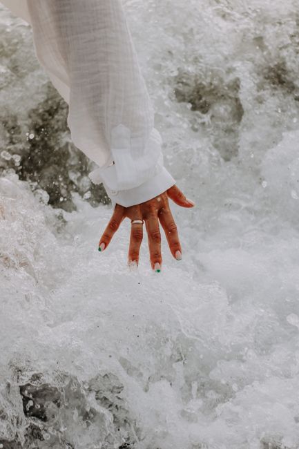Close-up of a hand in a white sleeve touching ocean waves, creating a splash.