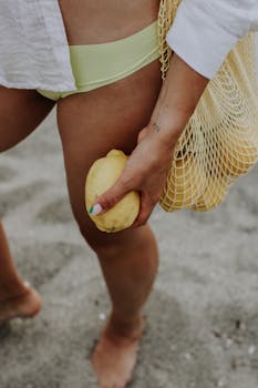 A person holds a lemon at the beach, wearing a net bag and swimwear.