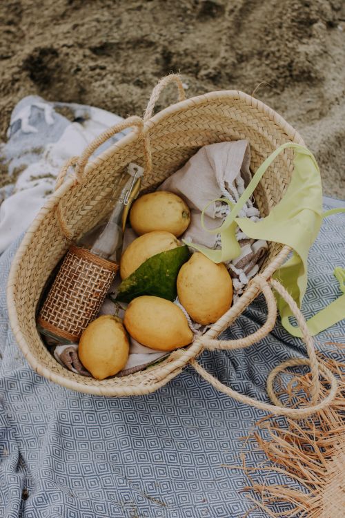 Free Straw basket filled with lemons on a blanket, perfect for a summer beach picnic. Stock Photo