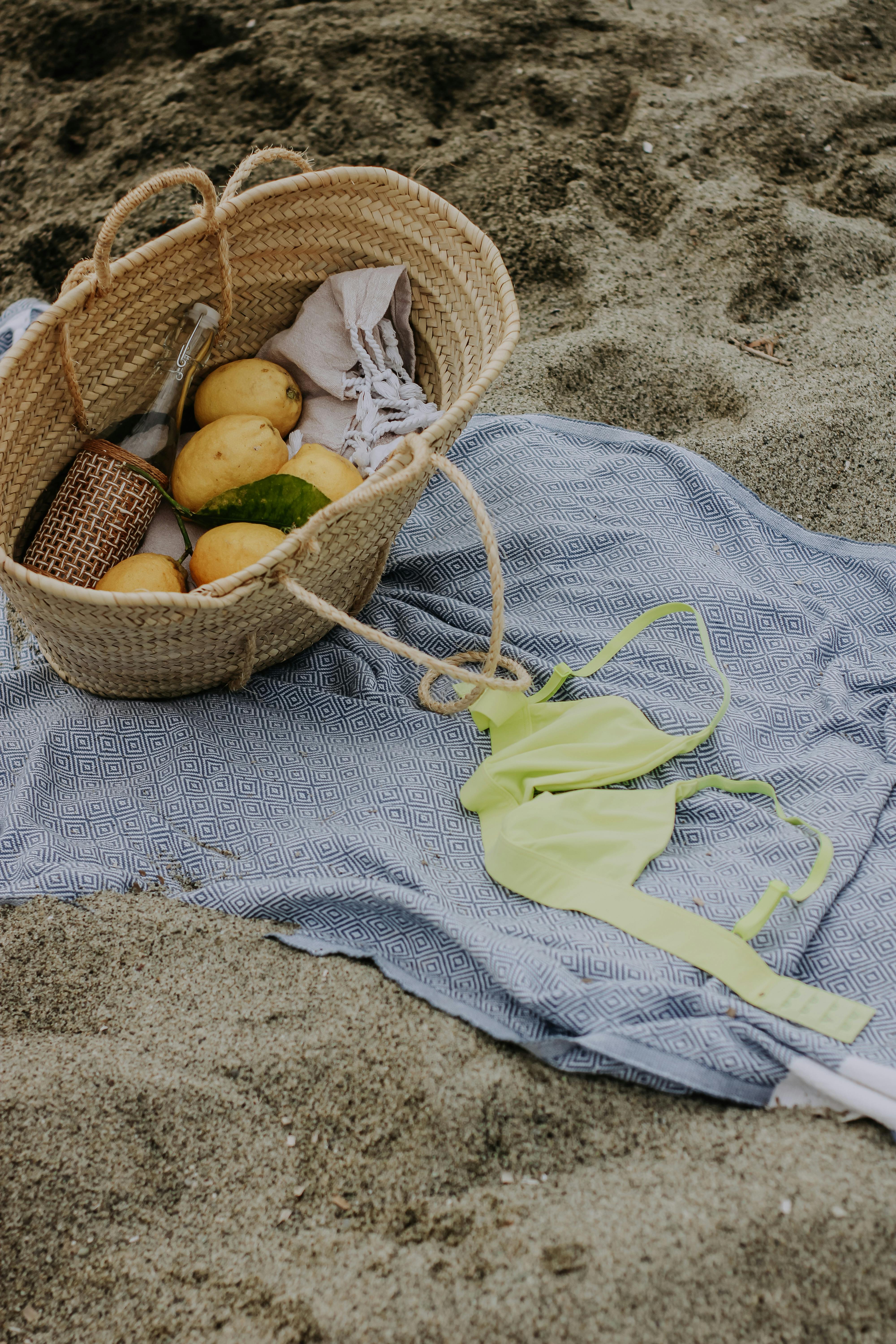 A beach setting with a basket of lemons, cloth, and swimwear on sand, ideal for summer vibes.