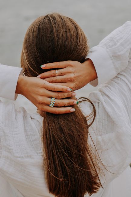 Back view of woman tying her hair with sandy hands on a beach.