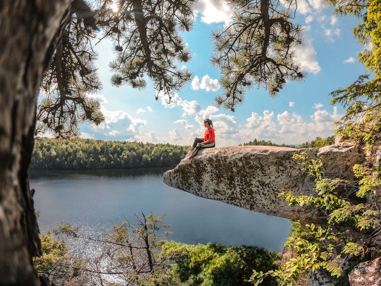 Girl Sitting On Rock Overhang Over Lake