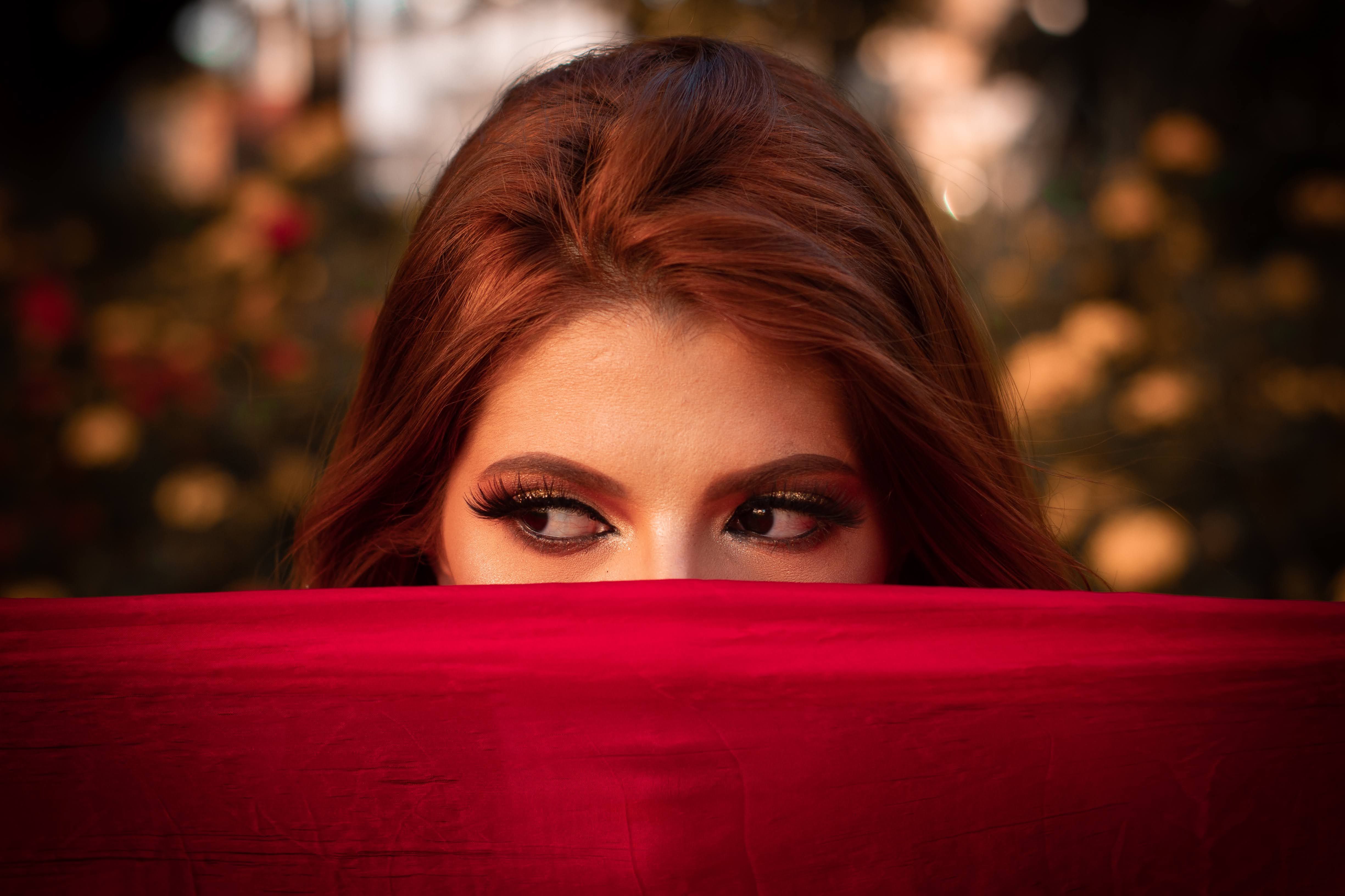 Close-up portrait of a woman with striking eyes partially concealed by a vibrant red cloth.
