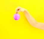 在明亮的黄色背景下，一只手握着紫色的苹果，形成了大胆的对比