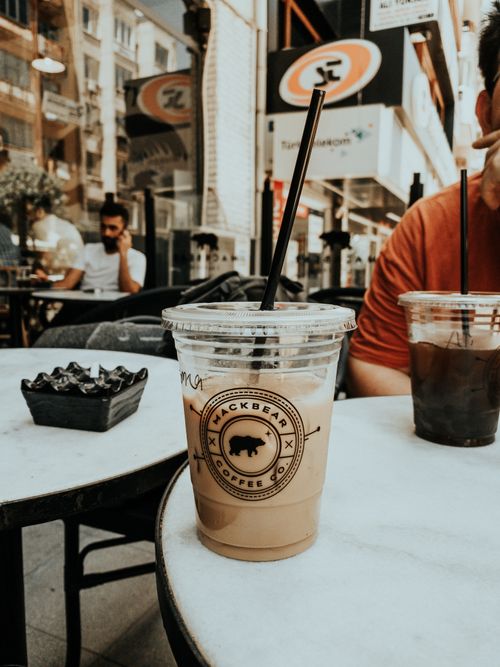 Free Close-up of iced coffee in plastic cup on outdoor cafe table with blurred street view. Stock Photo