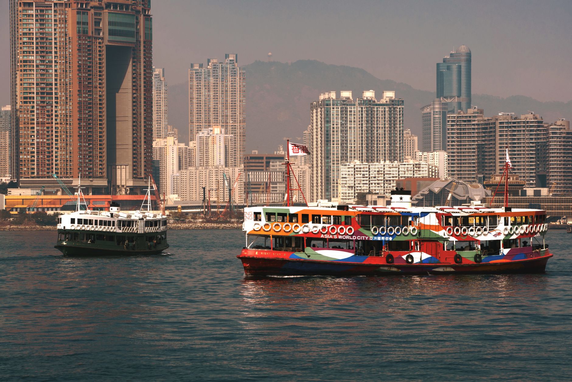 A vibrant ferry sails through Victoria Harbour with Hong Kong skyscrapers in the background.