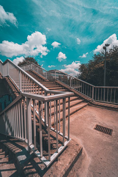 Free Serene view of a staircase leading up under a vibrant blue sky with fluffy clouds. Stock Photo