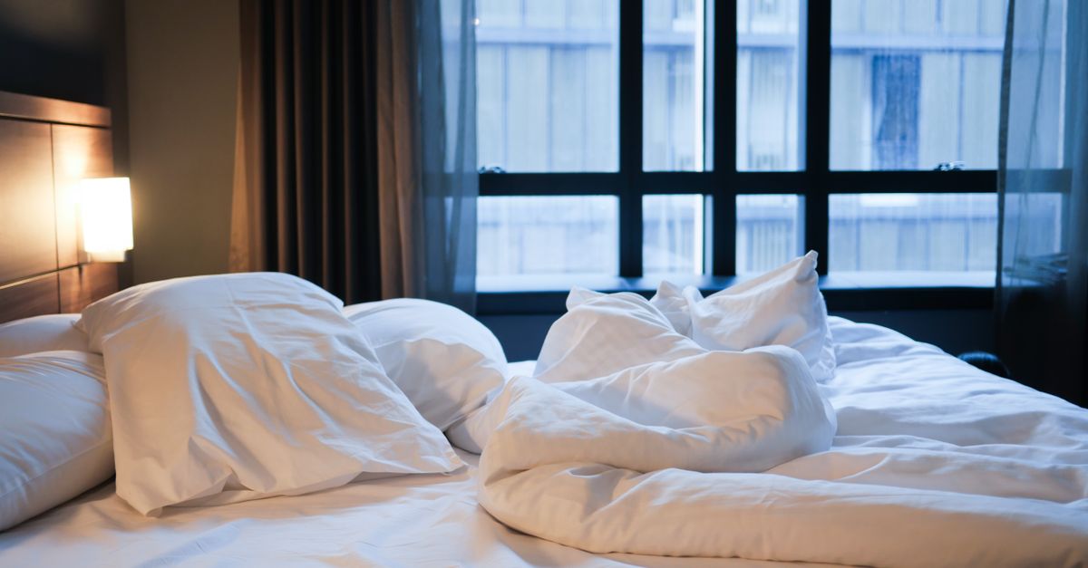 Uma cama confortável desarrumada com lençóis brancos e travesseiros em um ambiente de hotel contemporâneo.
