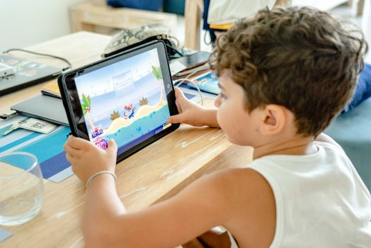 A young boy engrossed in playing a video game on a tablet at home.