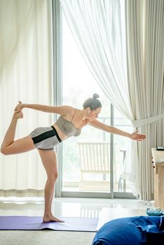 A woman in sports clothing performing yoga indoors with AirPods, showcasing fitness and balance.