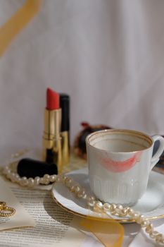 A stylish setup with a coffee cup marked with lipstick, surrounded by pearls and cosmetics.