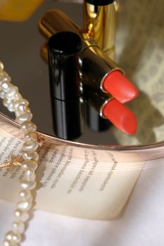 A sophisticated still life featuring red lipstick, a pearl necklace, and a mirror.
