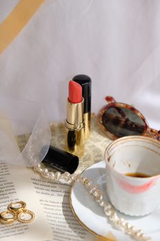 A stylish arrangement featuring lipstick, pearls, and a coffee cup on elegant decor.