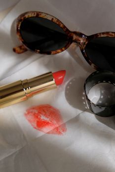 Stylish flat lay of sunglasses, lipstick, and film strip on white background.