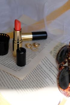 Chic arrangement of red lipstick, gold earrings, sunglasses, and text pages for beauty and fashion theme.