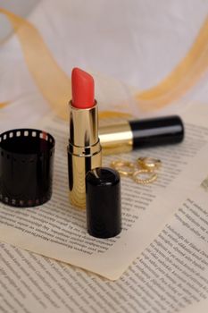 A vibrant lipstick with gold detailing sits elegantly on an open book, surrounded by film and jewelry.
