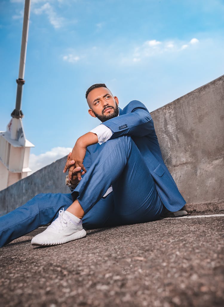 A Low Angle Shot Of A Man In Blue Suit And Pants Sitting On A Concrete Floor