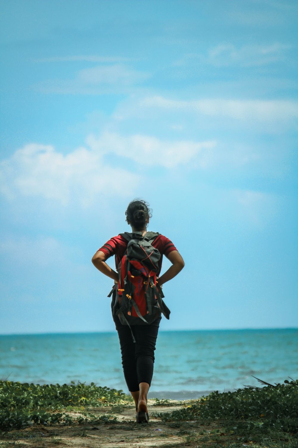 Woman with a backpack walking toward the sea on a sunny beach day