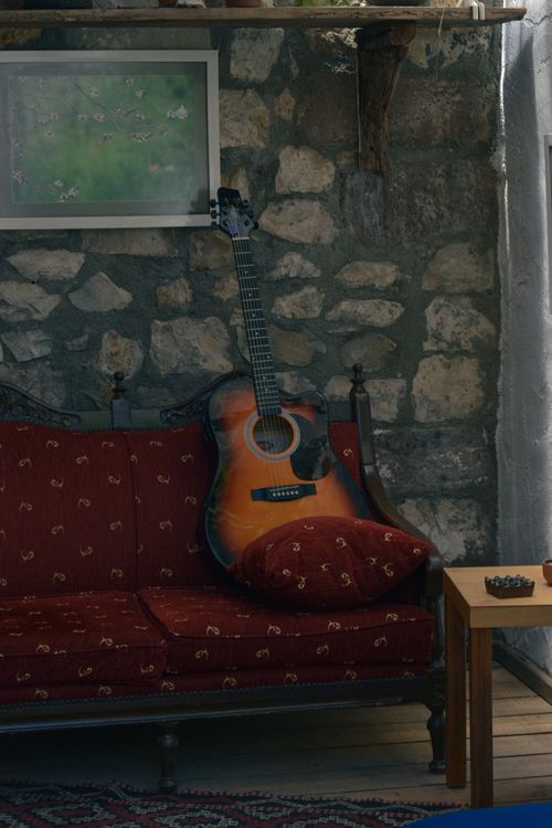 Free A cozy living room with an acoustic guitar on a couch against a rustic stone wall. Stock Photo