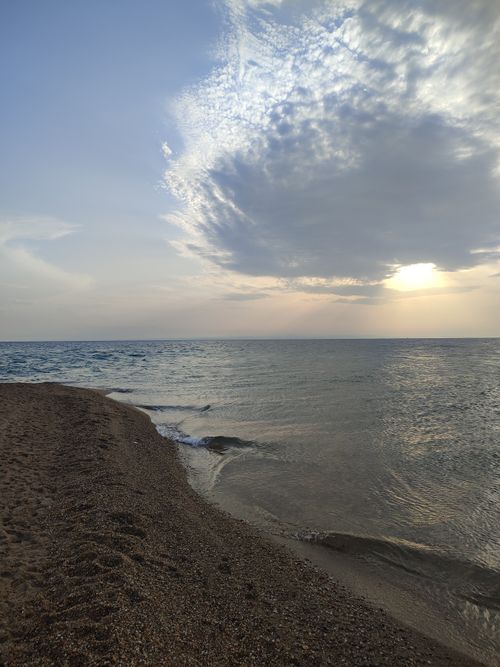 Free Capture the serene beauty of a sunset over a peaceful beach with gentle waves and a cloudy sky. Stock Photo