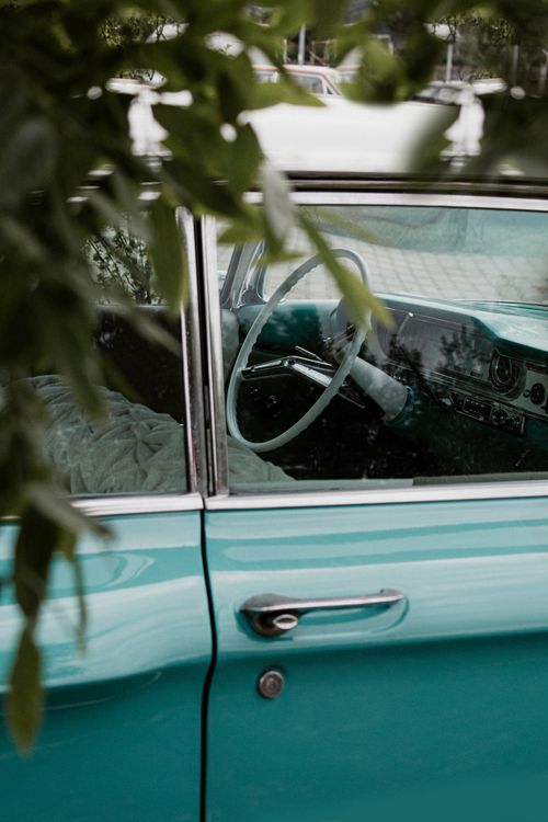 Free Close-up of a classic turquoise car, partially obscured by leaves, showcasing the car's interior and door handle. Stock Photo