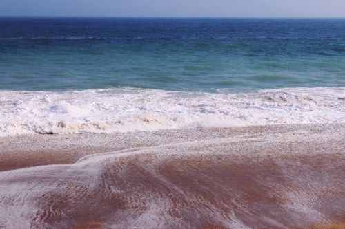 Free Peaceful ocean waves gently crashing on the sandy shore under a clear sky. Stock Photo