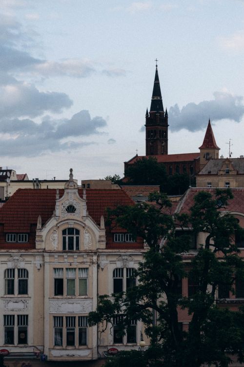 Free View of Gothic church tower and historic buildings under cloudy skies. Stock Photo