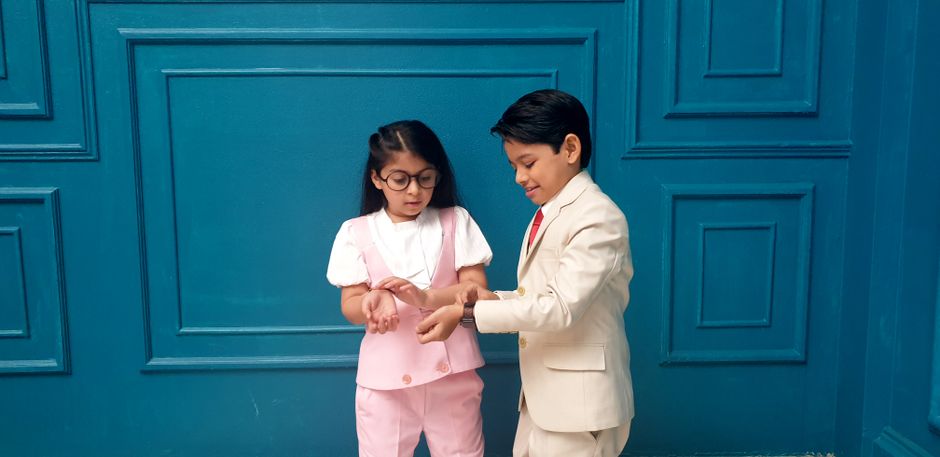 Two children in formal clothing standing together with a blue backdrop.