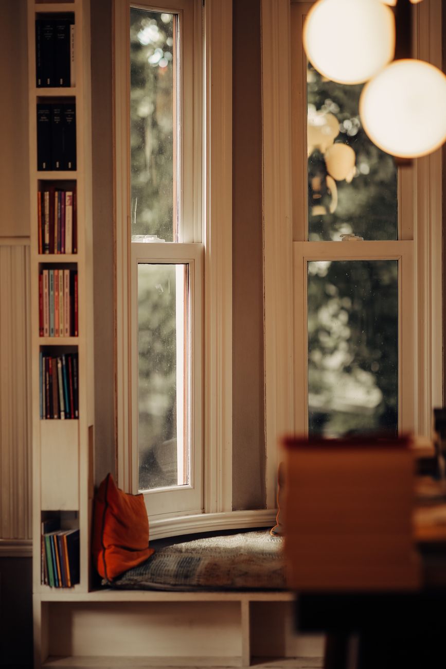 Warm and inviting reading nook by windows, ideal for relaxation and book lovers.