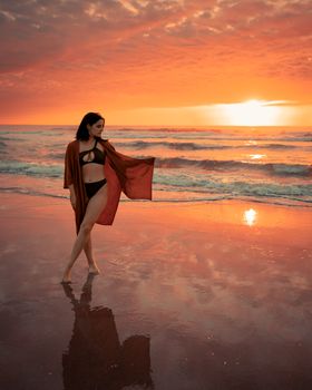 A woman poses gracefully on a beach at sunset, embracing the vibrant orange hues.