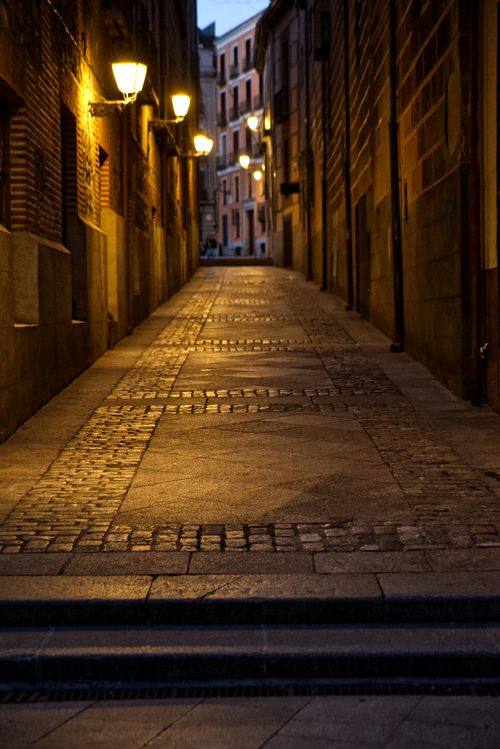 Free A moody cobblestone alley illuminated by street lamps, evoking a serene urban night scene. Stock Photo