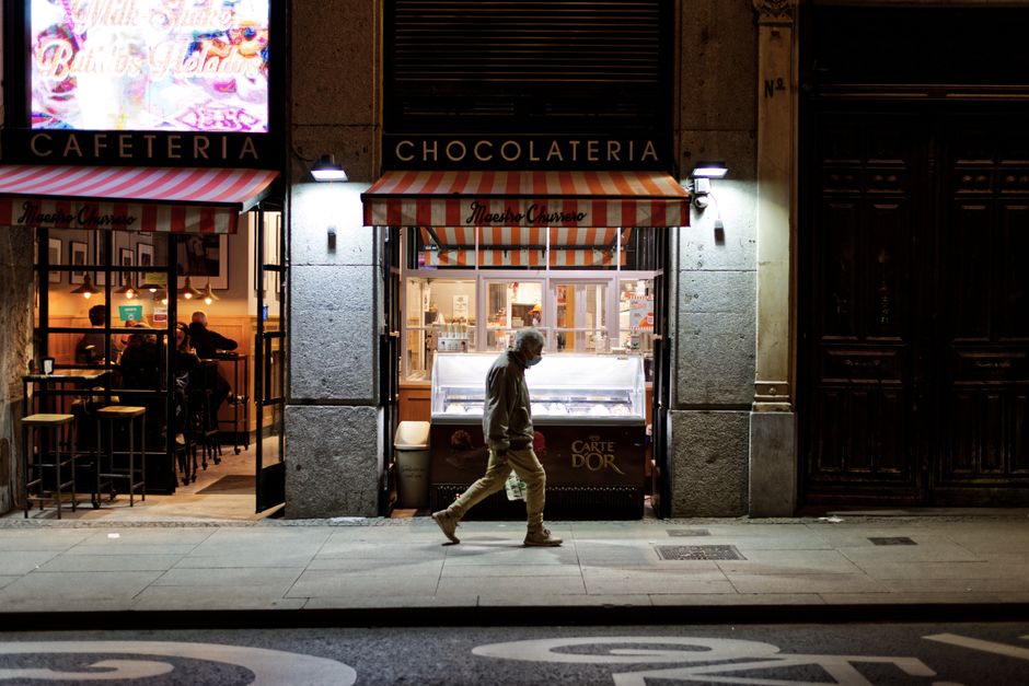 Un hombre anciano pasa por una cafetería y chocolatería bien iluminada por la noche.
