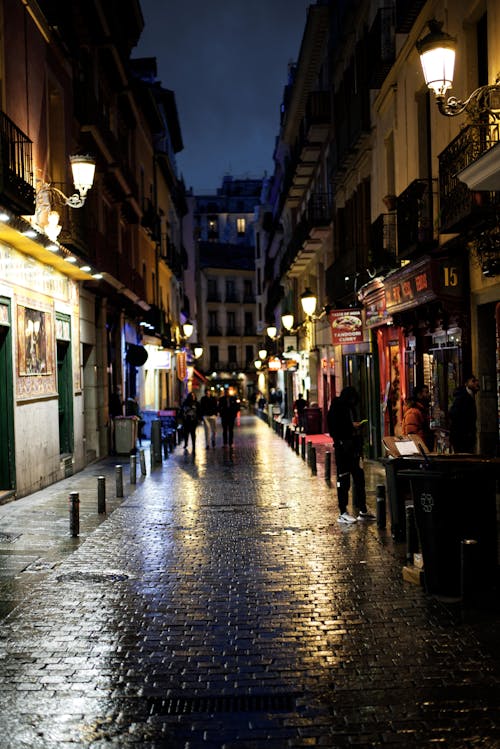 Free A picturesque evening on a European cobblestone street illuminated by street lamps and bustling with people. Stock Photo