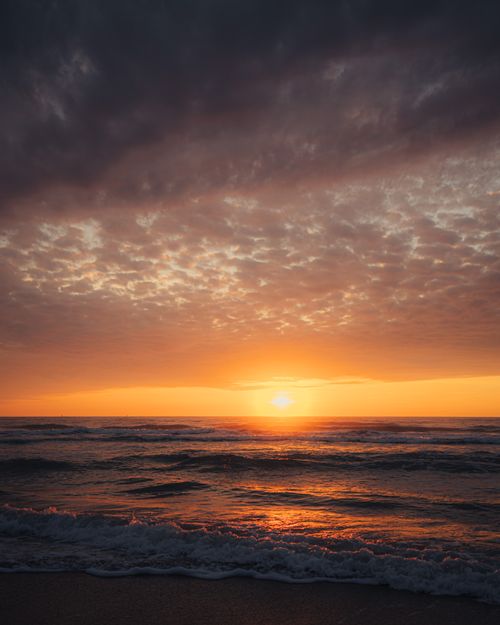 Free Stunning sunset over the ocean with dramatic clouds and vibrant hues. Stock Photo