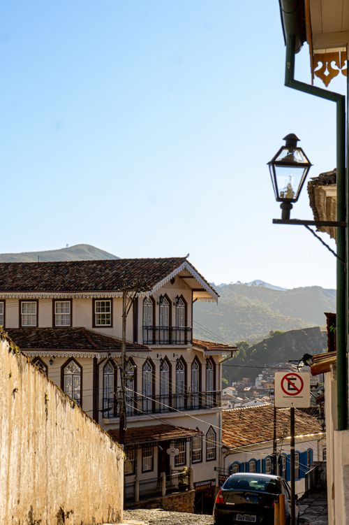 Free A picturesque view of a colonial town street with traditional architecture and mountain backdrop. Stock Photo