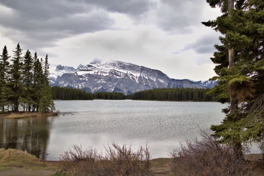 Scenic view of snow-capped mountains and lake in Banff National Park, Canada, under a cloudy sky.