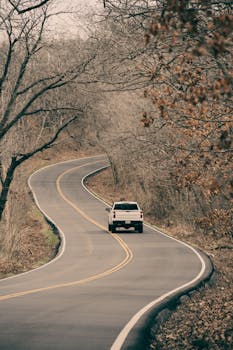 A lone vehicle travels a winding road amidst bare trees, showcasing the tranquil beauty of a Missouri landscape in winter.