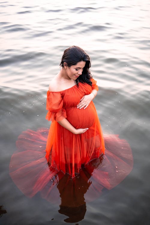 A Pregnant Woman in Red Dress Standing on Water